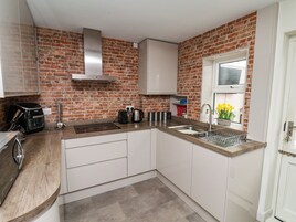 Una cocina con gabinetes blancos, pared de ladrillo, extractor de acero inoxidable, un lavamanos y una ventana con flores.