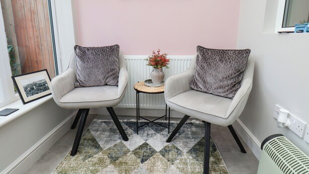 Une pièce comprenant deux fauteuils, une petite table, un tableau encadré et un radiateur.