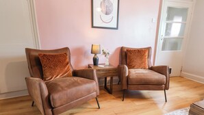 A room with two brown leather chairs, a small wooden table with a lamp, a vase with flowers, and a framed picture on the wall. - The Braes (Redcar)