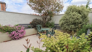 A patio with a table and chairs, surrounded by various plants and a tree. - The Braes (Redcar)