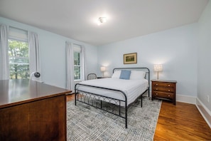 Ein Schlafzimmer mit einem Bett, Nachttischen, einem Schreibtisch und einem Vorhangfenster.