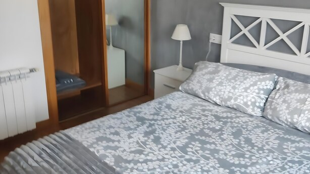 A bedroom with a bed, a wardrobe, a nightstand, and a lamp.