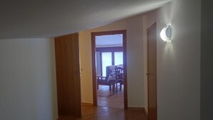 A hallway with wooden flooring leading to a room with a bed and a chair.