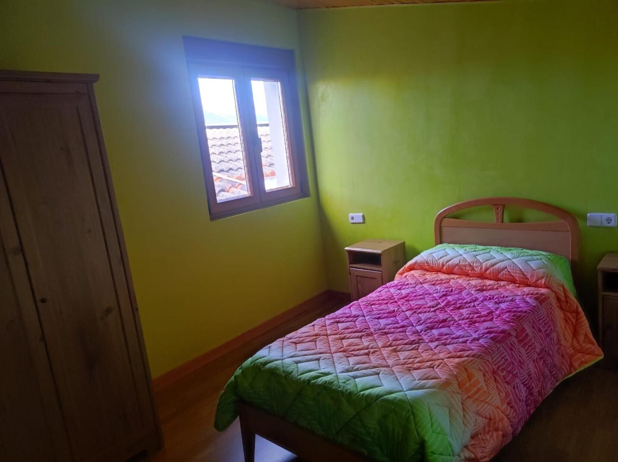 A room with a bed, a window, a wooden wardrobe, and a nightstand.