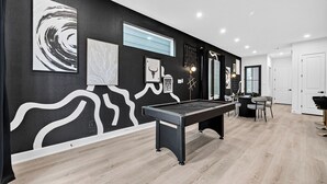 Ein modernes Zimmer mit Billardtisch, Kunstwerken an der Wand und einem Essbereich.
