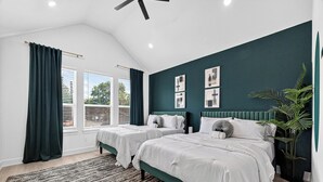 Ein Schlafzimmer mit zwei Betten, einem Deckenventilator, einem großen Fenster mit Vorhängen und einer Wand in Grünton.