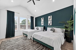 Ein Schlafzimmer mit zwei Betten, einem Deckenventilator, einem großen Fenster mit Vorhängen und einer Wand in Grünton.