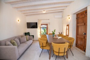 Un comedor con una mesa de madera y sillas amarillas, un sofá y un televisor montado en la pared.