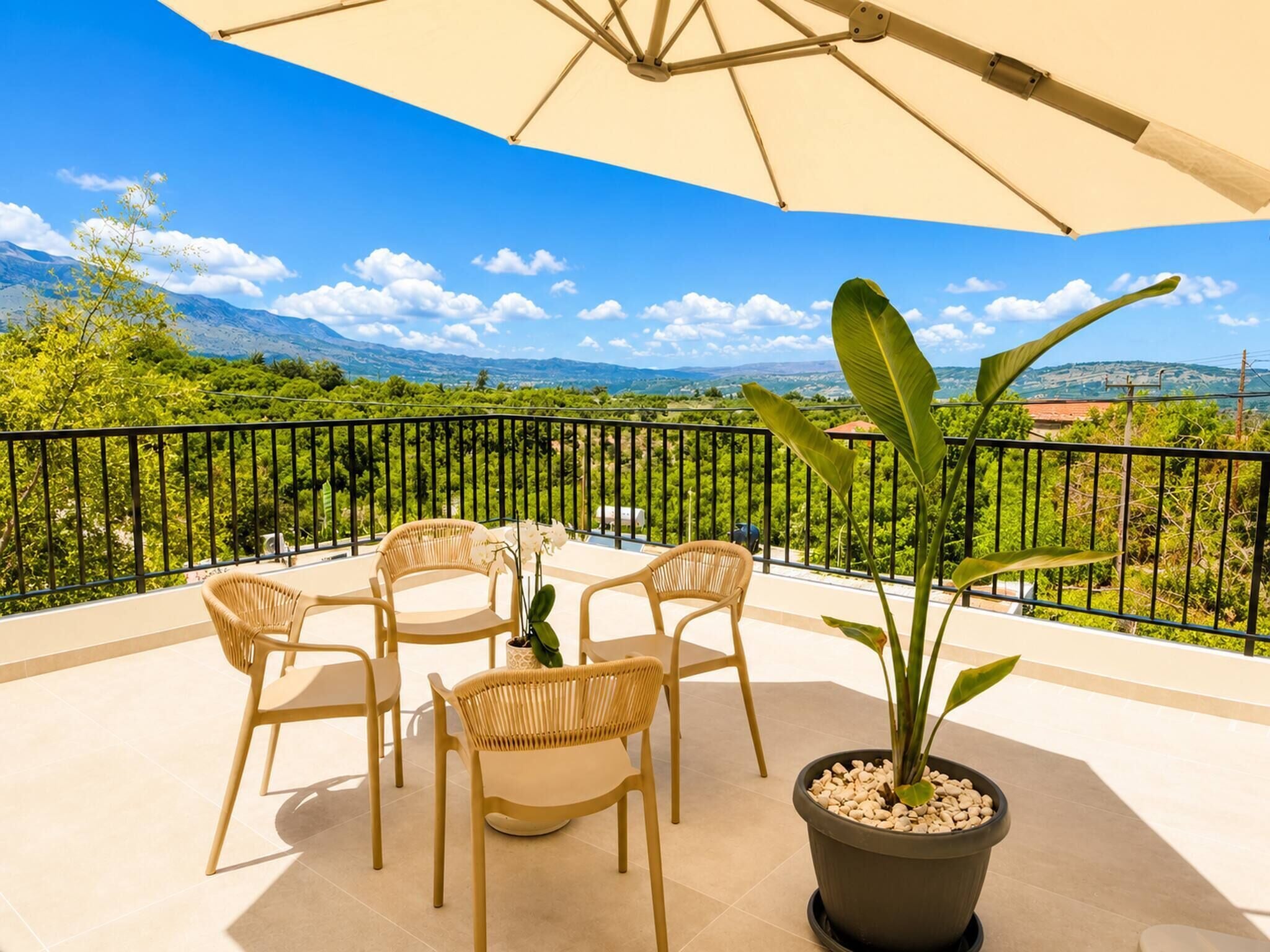 A balcony with a table and chairs, a potted plant, and a view of mountains and greenery.