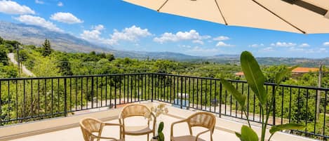 A terrace with a table and chairs, a potted plant, and a view of mountains.
