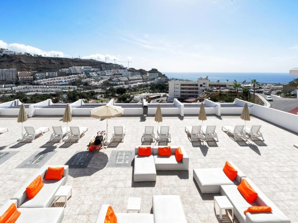 Terraço no telhado com cadeiras de lounge brancas e almofadas laranja, com vista para o horizonte costeiro.