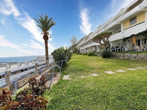 A hotel with a grassy courtyard, a palm tree, and a view of the sea.