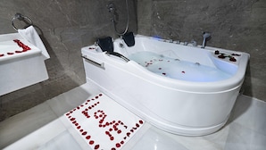 A modern bathroom with a freestanding bathtub, a towel rack, and a rose petal arrangement on the floor. - Romantic Honeymoon Suite in Heart of Jeddah (Jeddah)