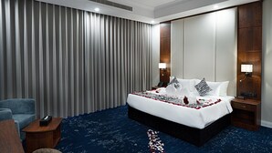 A hotel room with a large bed, a bedside table with a lamp, a chair, a desk with a phone, and a large window with curtains. - Romantic Honeymoon Suite in Heart of Jeddah (Jeddah)