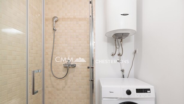 A bathroom with a shower, a white wall-mounted heater, and a front-loading washing machine. - Refined 1bd apartment with outdoor pool (Budva)