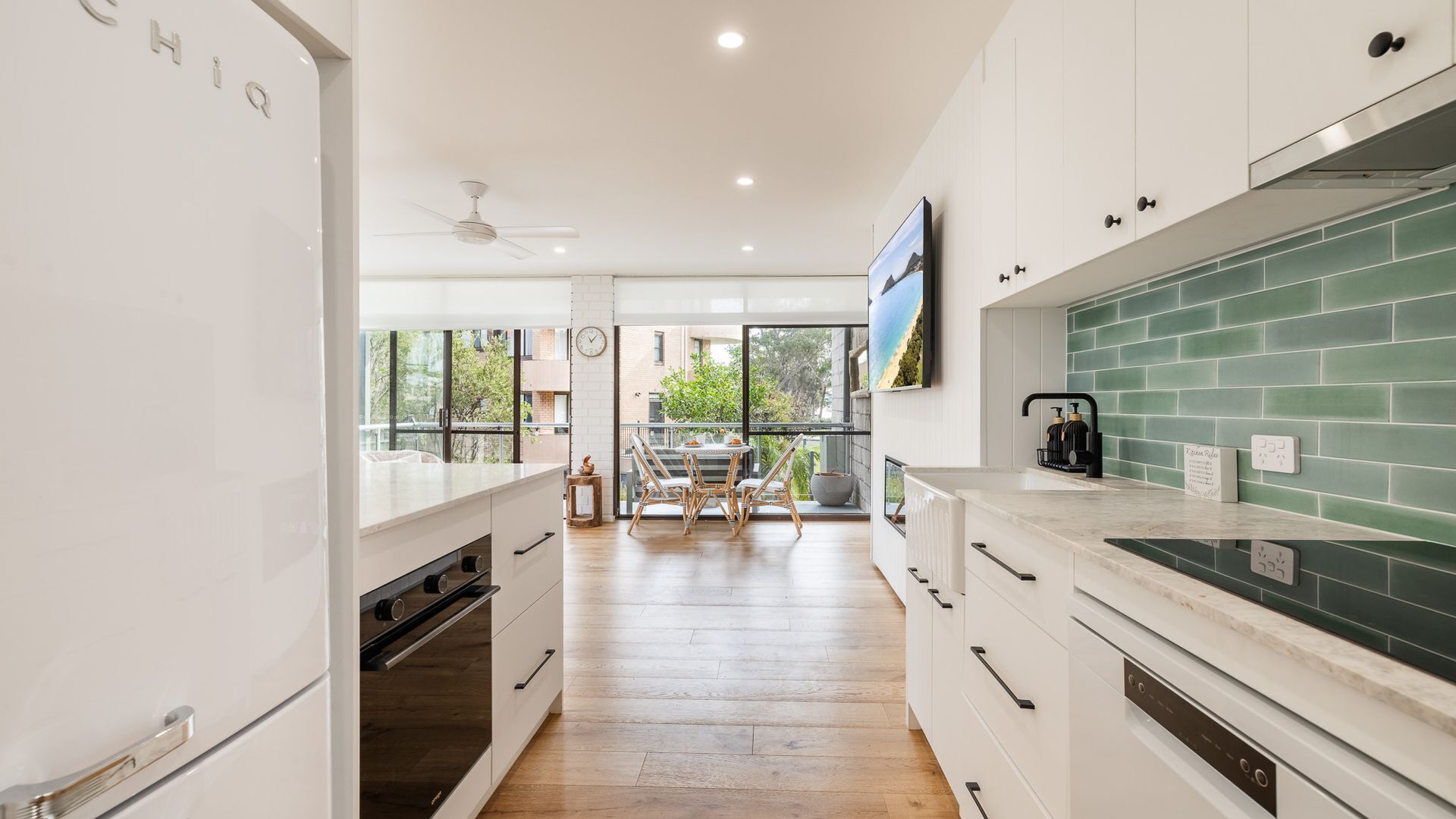 A modern kitchen with white cabinetry, a green backsplash, and a dining area with natural light.
