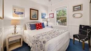 A bedroom with a bed, a chair, a window, and wall art. - Magical Coastal Cottage, Short Walk to Beach by Tybee Cottages (Tybee Island)