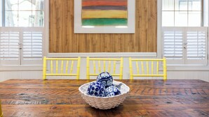 A dining table with a bowl of decorative items, wooden paneled walls, and two windows with shutters. - Magical Coastal Cottage, Short Walk to Beach by Tybee Cottages (Tybee Island)