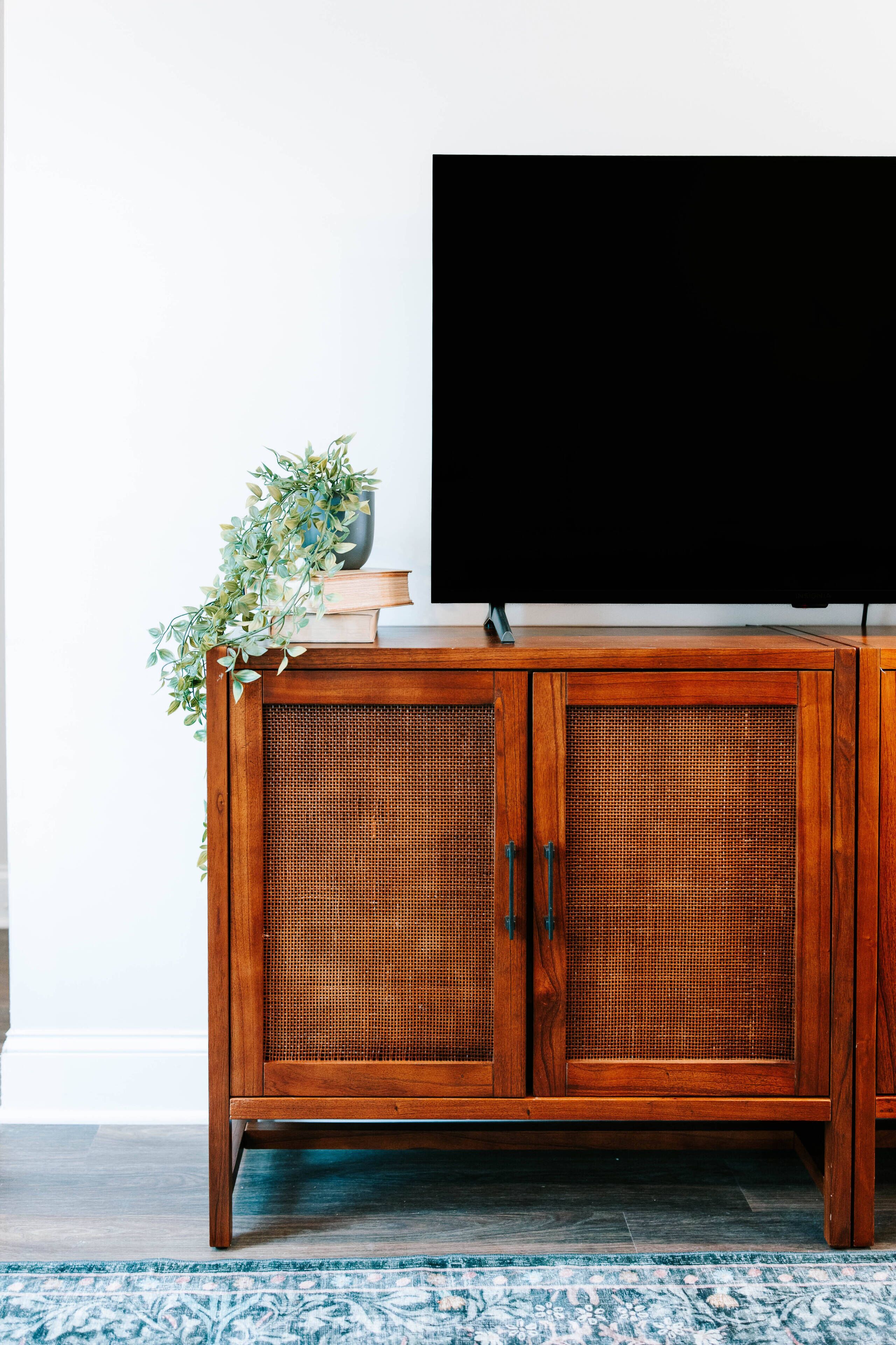 A wooden cabinet with a television on top, a plant, and a woven basket.
