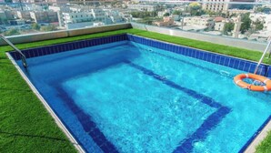 Una piscina en la azotea con agua azul cristalina, rodeada por un borde de baldosas y una franja de césped.