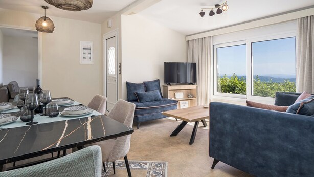A modern living room with a dining area, a sofa, a TV, and a large window with a view. - 3-bedroom eco villa in excellent Dilinata, family / friends friendly (Dilinata)