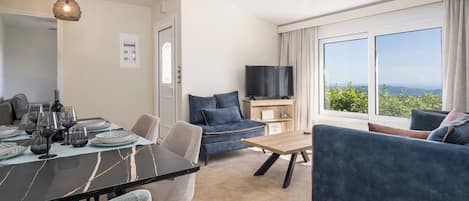 En moderne stue med spiseplads, sofa, fjernsyn og et stort vindue med udsigt.
