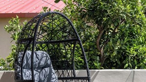 A wicker chair with cushions, a small round table with a drink and fruit, and a red-roofed building in the background. - 3-bedroom eco villa in excellent Dilinata, family / friends friendly (Dilinata)