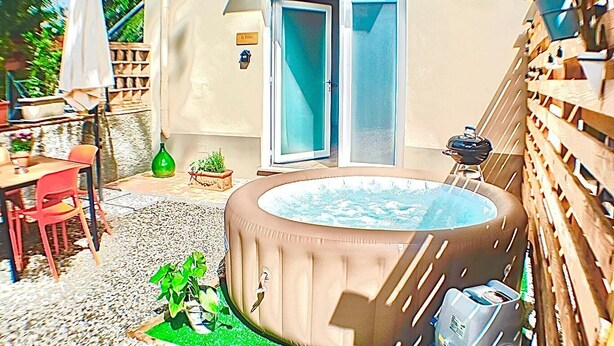 Uma banheira de hidromassagem em um quintal com uma mesa e cadeiras de pátio, uma porta de vidro deslizante e um cercado de madeira.