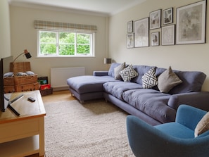 A living room with a sofa, armchairs, a coffee table, a lamp, a radiator, a window with blinds, and framed artwork on the wall.