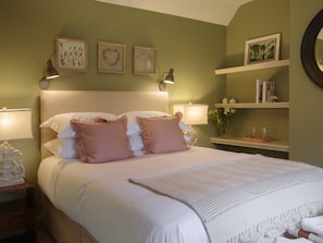 Una cama bien hecha con almohadas, una lámpara de noche e impresiones botánicas enmarcadas en la pared.