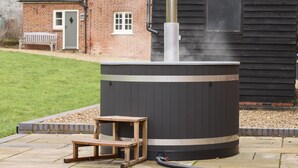 Un jacuzzi con un banco de madera al frente, una casa de ladrillo al fondo y un cobertizo de madera.