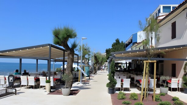 Un restaurante frente al mar con terraza, plantas en macetas y vistas despejadas al océano.