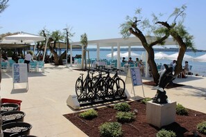 En patio ved stranden med udendørs møbler, cykler og en skulptur.