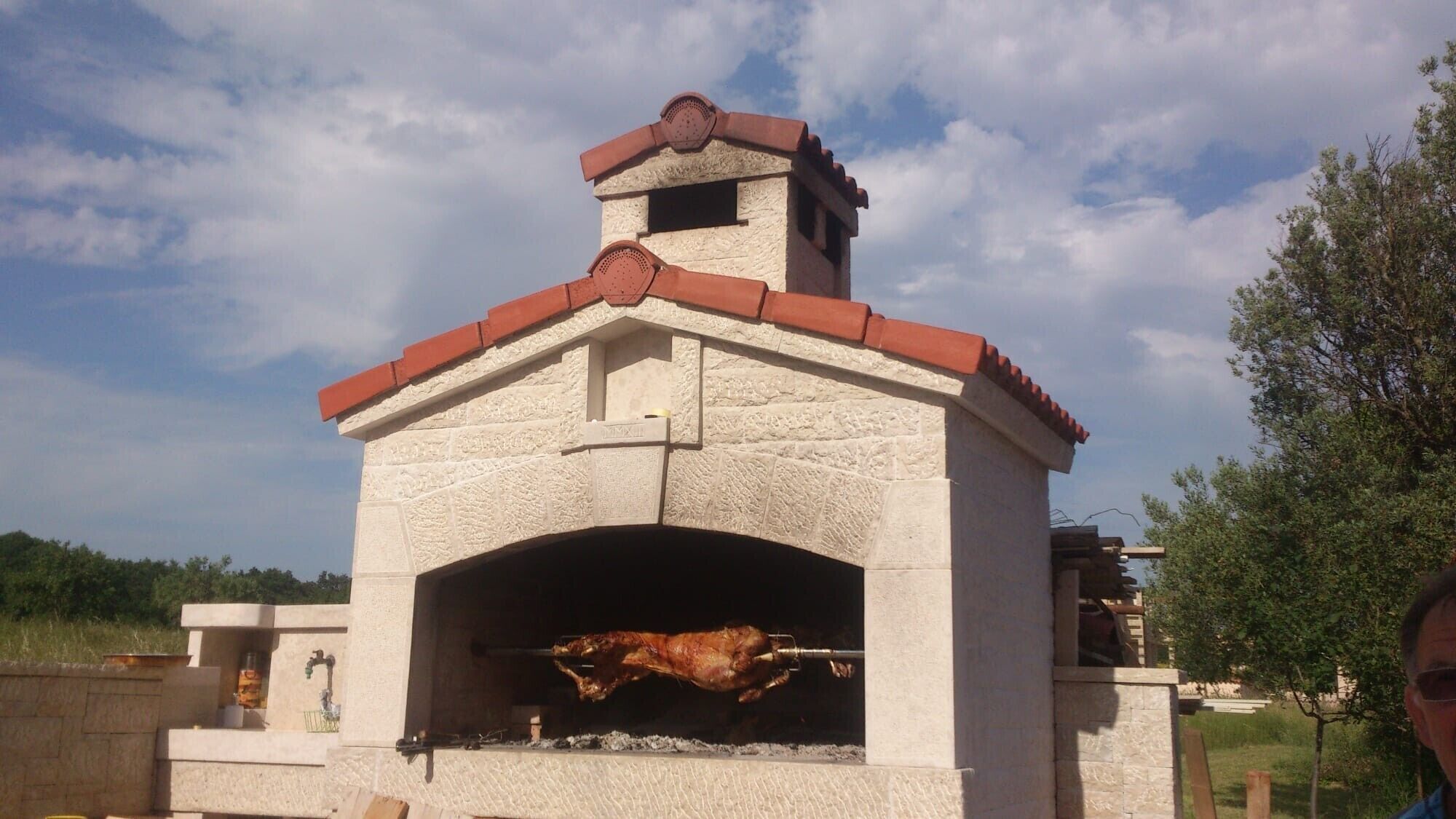 Un four à rôtir traditionnel en pierre, installé à l’extérieur, doté d’une cheminée et d’une petite fenêtre.