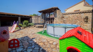 Eine Steinterrasse mit Trampolin, kleinem Pool und einem Spielhäuschen für Kinder.