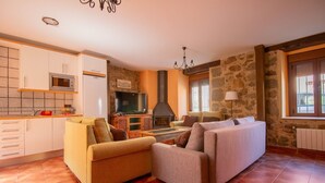 Ein Wohnzimmer mit Kamin, Sofas, einem Fernseher und einer Küchenzeile.