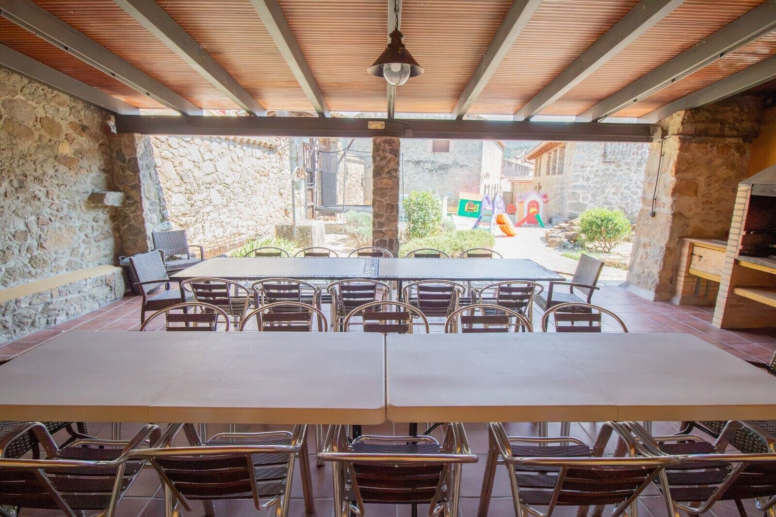 Un patio al aire libre con pared de piedra, techo de madera y vista a una calle con edificios y un mural colorido.