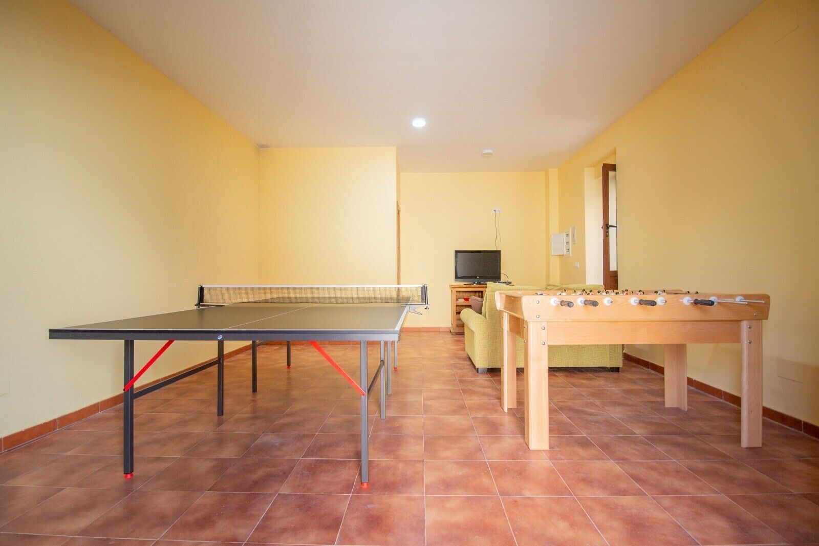 Una habitación con mesa de ping pong, mesa de fútbol, sofá y televisor.