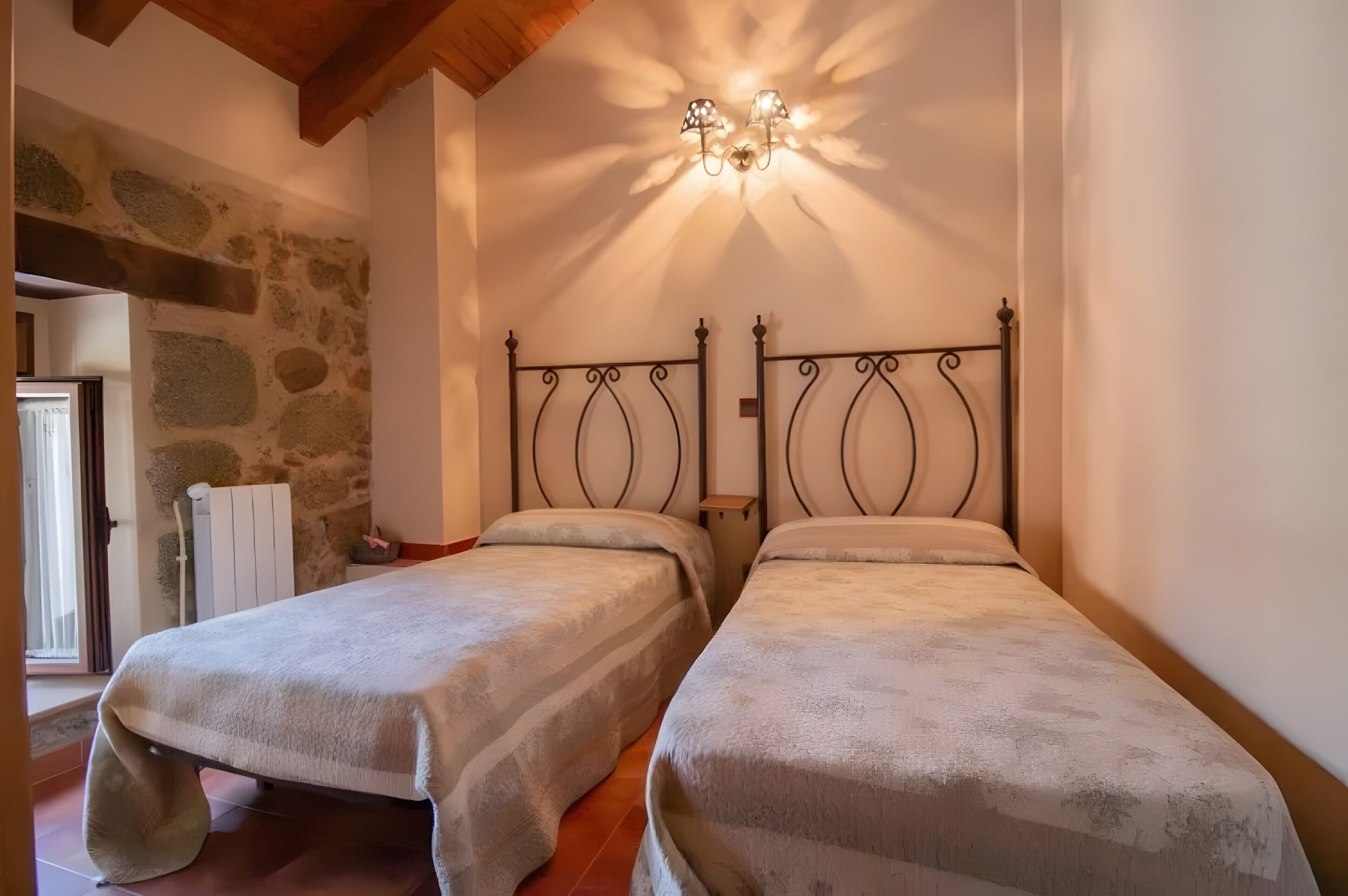 Una habitación con dos camas, una pared de piedra, techo de madera y un radiador.