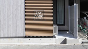 A modern building with a wooden slatted facade, a visible entrance, and a bicycle parked outside. - Koti Sopo Universal Bay 2 by Liaison (Osaka)