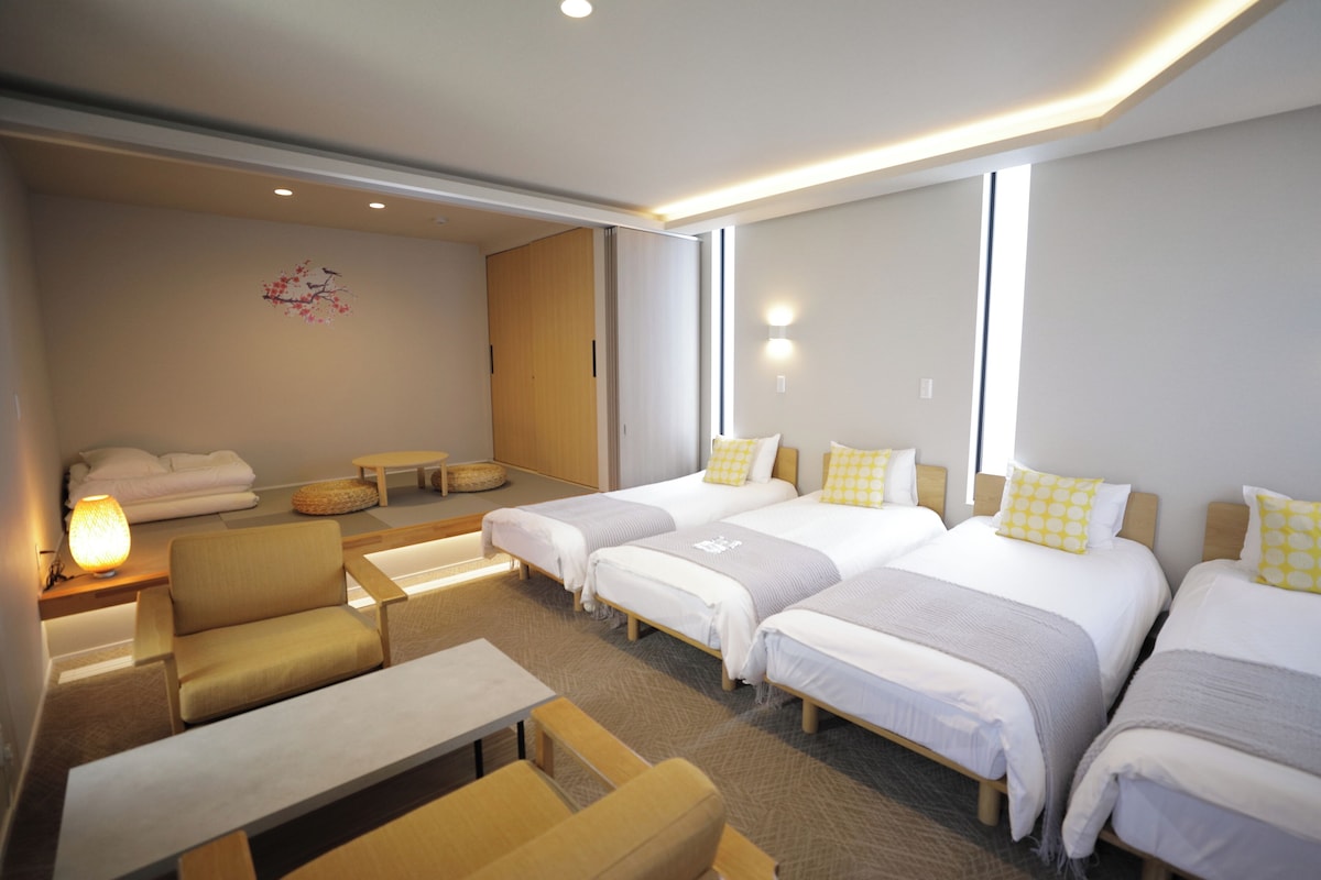 Une chambre d’hôtel avec quatre lits, un canapé, une table et une lampe.