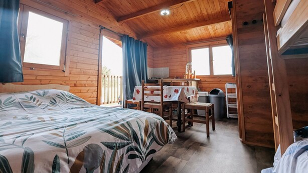 Une cabane en bois avec un lit, une table, une chaise et un téléviseur.