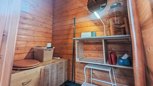 L’intérieur d’une cabane en bois, avec un plancher en bois, un banc en bois, une petite table sur laquelle se trouve une tasse, une échelle et une étagère avec un bocal et une boîte.