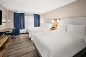 Ein Hotelzimmer mit zwei Betten, einem Schreibtisch, einem Sessel und einem Fernseher.