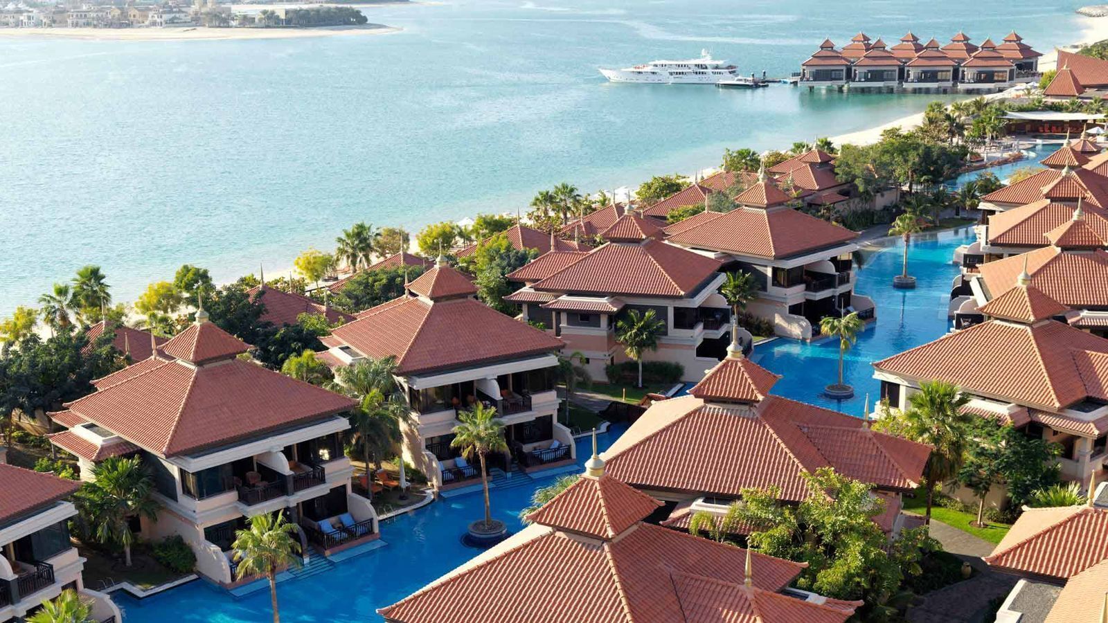 Un resort con varias edificaciones, una piscina central y vista al mar.
