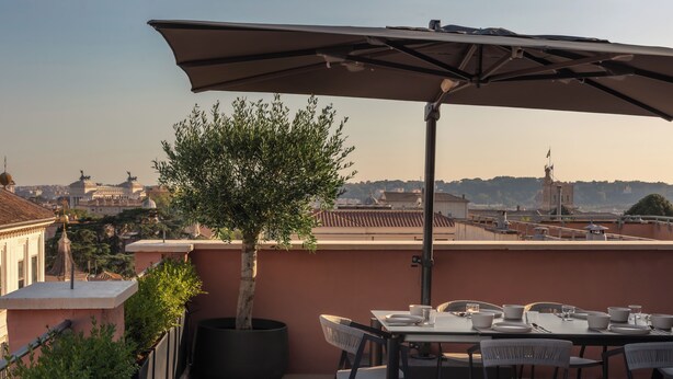 Una terraza con una mesa lista para comer, un árbol en maceta y vistas a edificios distantes.
