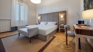 Una habitación de hotel moderna con una cama grande, un escritorio, una silla, una lámpara y una ventana con cortinas.