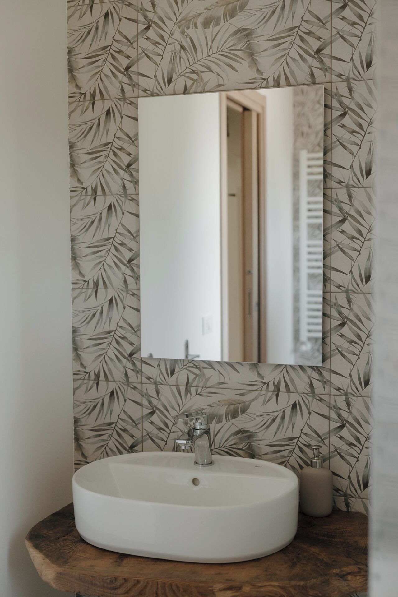 Ein Badezimmer mit einem runden Waschbecken, einem Spiegel und einer Wand mit einem Blattmuster.
