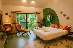 A hotel room with a bed, a desk, a chair, a window with curtains, and a view of greenery.