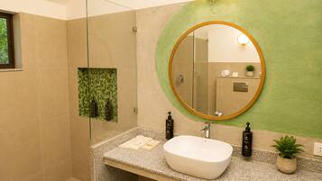 Un baño moderno con cabina de ducha de vidrio independiente, un lavamanos independiente sobre encimera de granito y un espejo redondo con marco dorado.